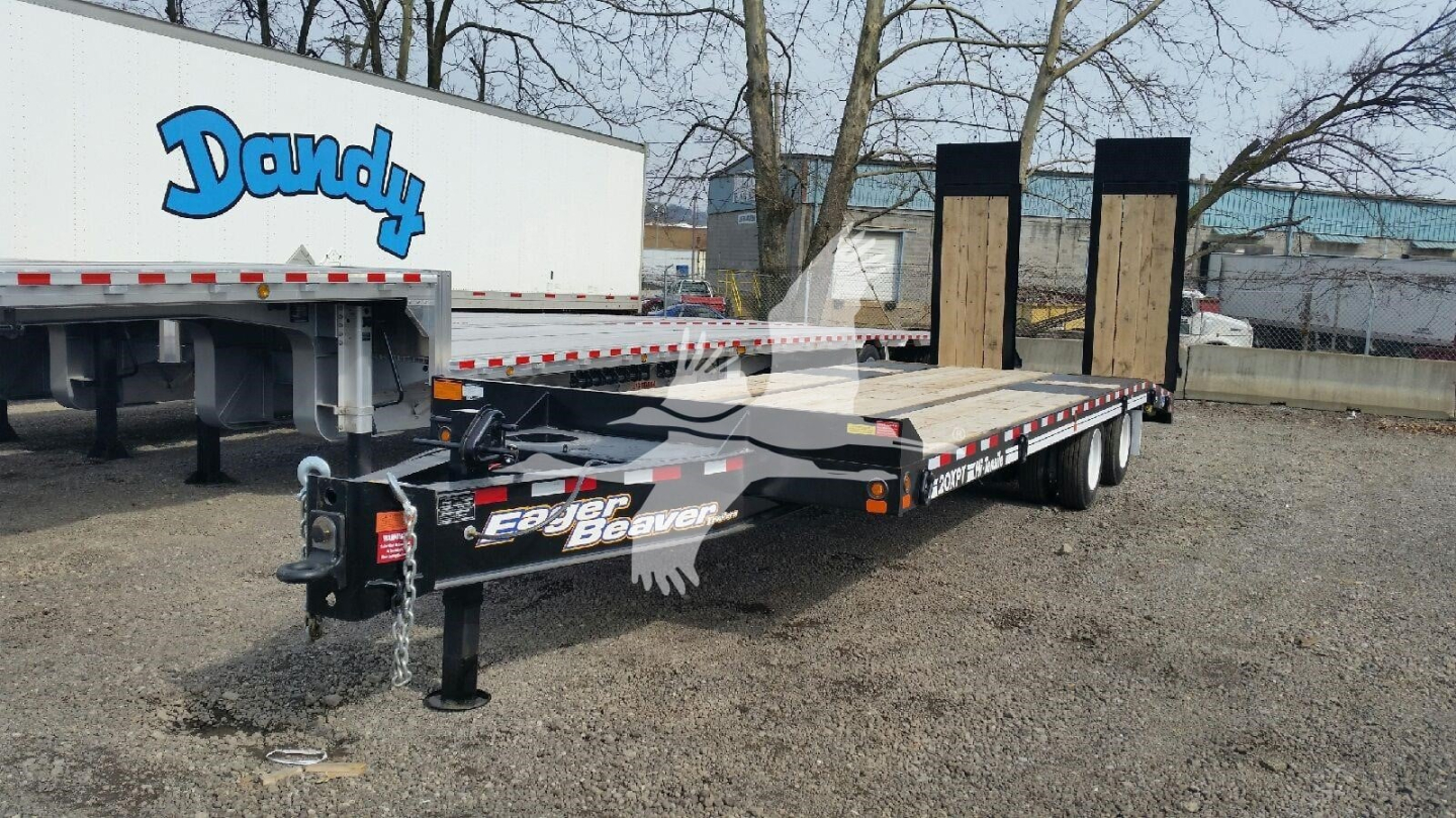 Trailer showing flatbed design with dual rear ramps and black frame; Eager Beaver branding on the frame; VIN and stock details visible on the truck nearby.