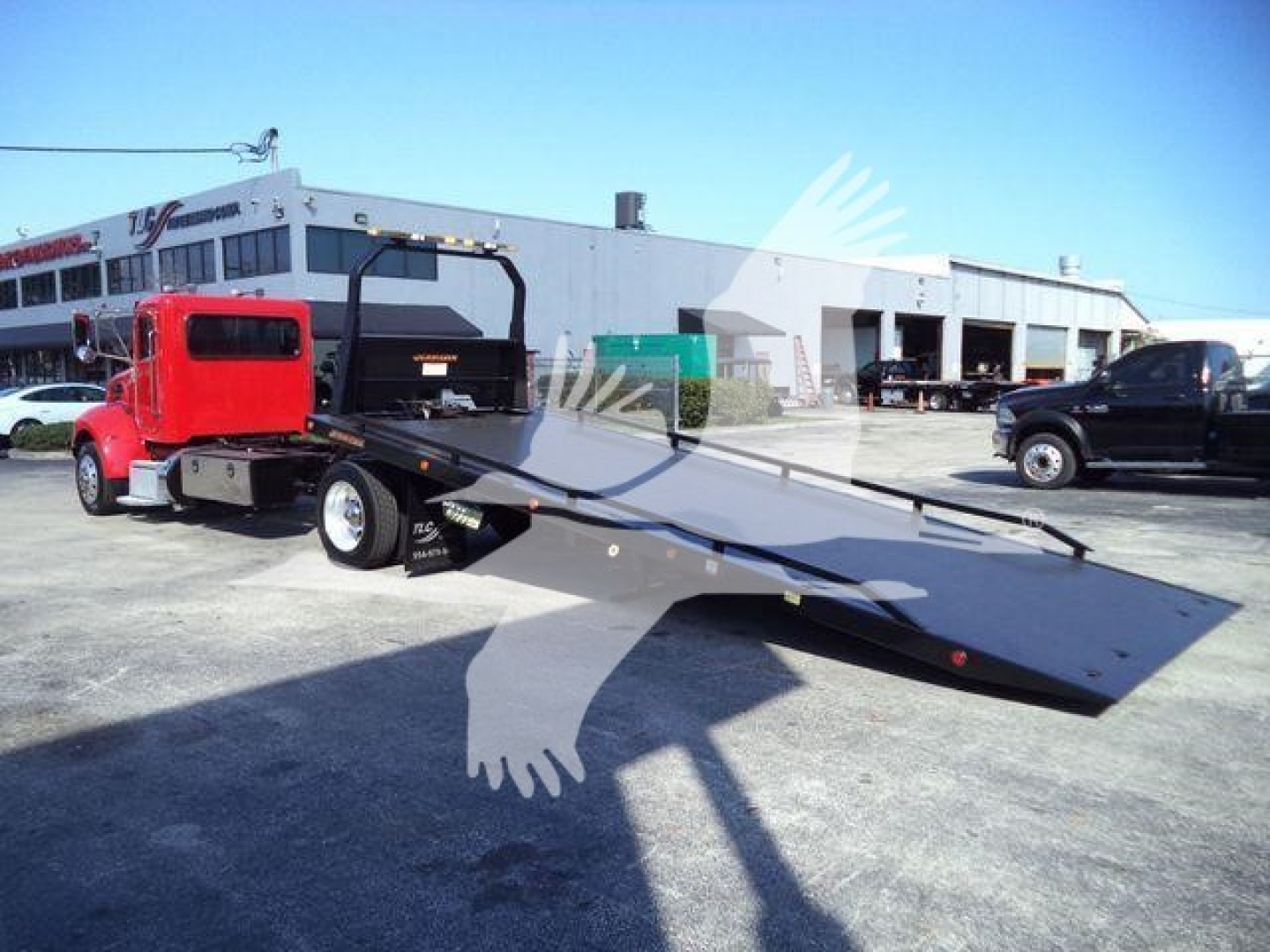 Peterbilt 337 rollback tow truck with flatbed and red cab in outdoor lot.