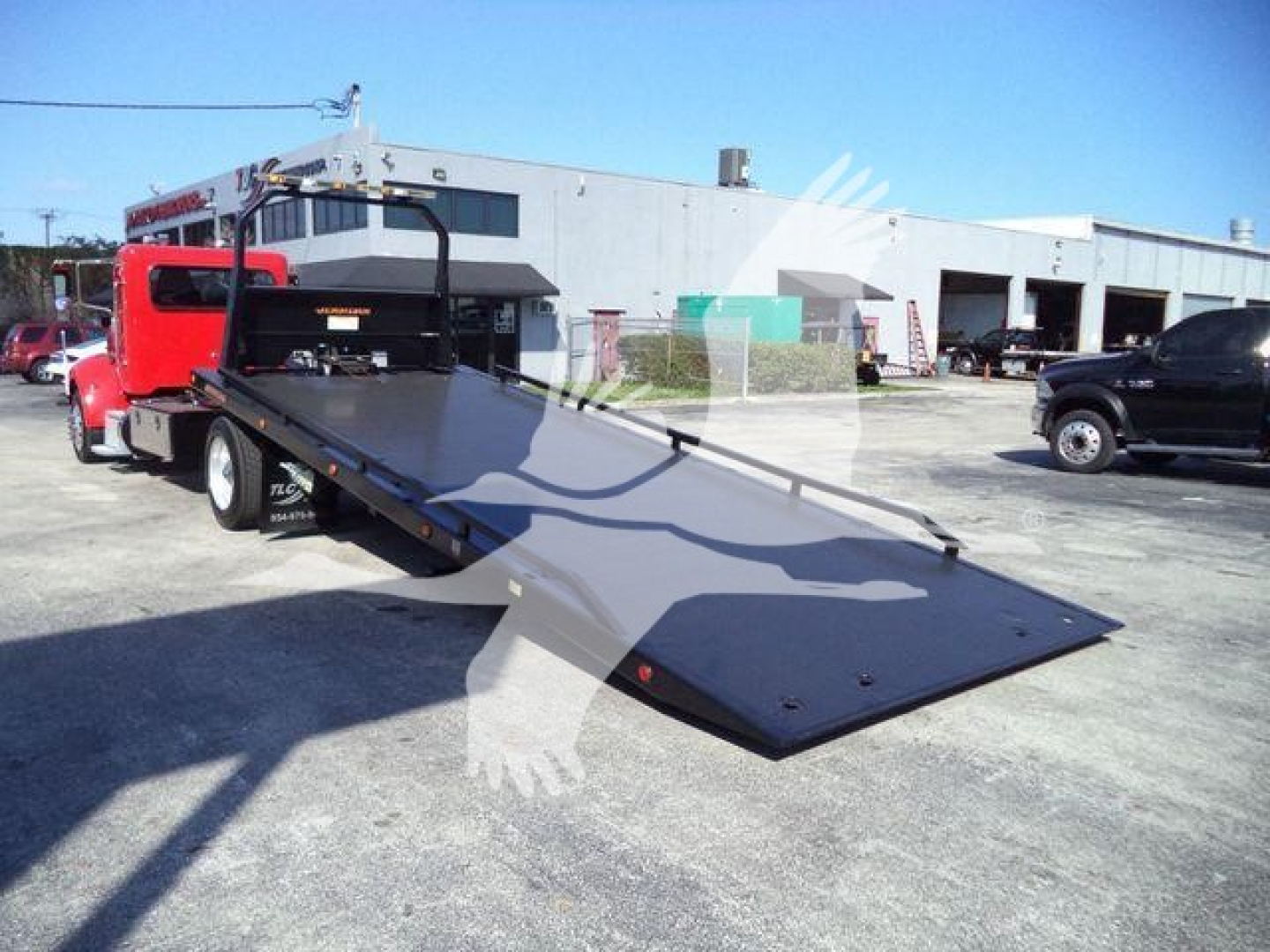 Peterbilt 337 rollback with lowered flatbed ramp in foreground; red cab, industrial yard background