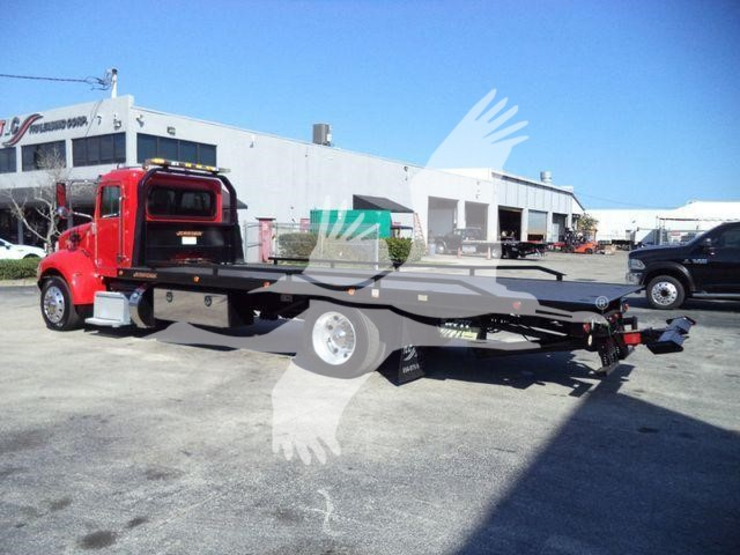 Red Peterbilt 337 rollback tow truck with flatbed in service lot; visible text on the building in background; no legible close-up text on the truck itself.