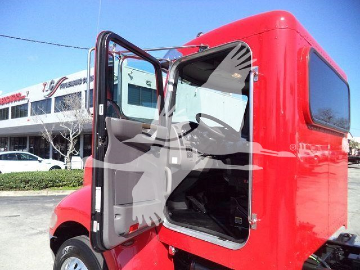 Peterbilt 337 rollback truck side cab open door showing interior seating and step, red exterior, dealership lot in background.