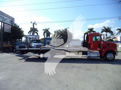 Truck-mounted rollback tow truck with a red cab and long flatbed in a parking lot, 2020 Peterbilt 337, stock number T56588FM.