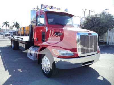 Peterbilt 337 rollback truck with red cab and flatbed, front grille and chrome bumper visible, daylight outdoor lot.