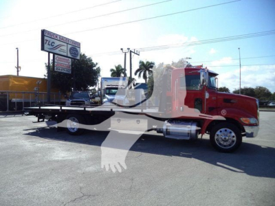 2020 Peterbilt 337 rollback tow truck side view showing flatbed, red cab, chrome fuel tanks, and wipers with dealership in background.