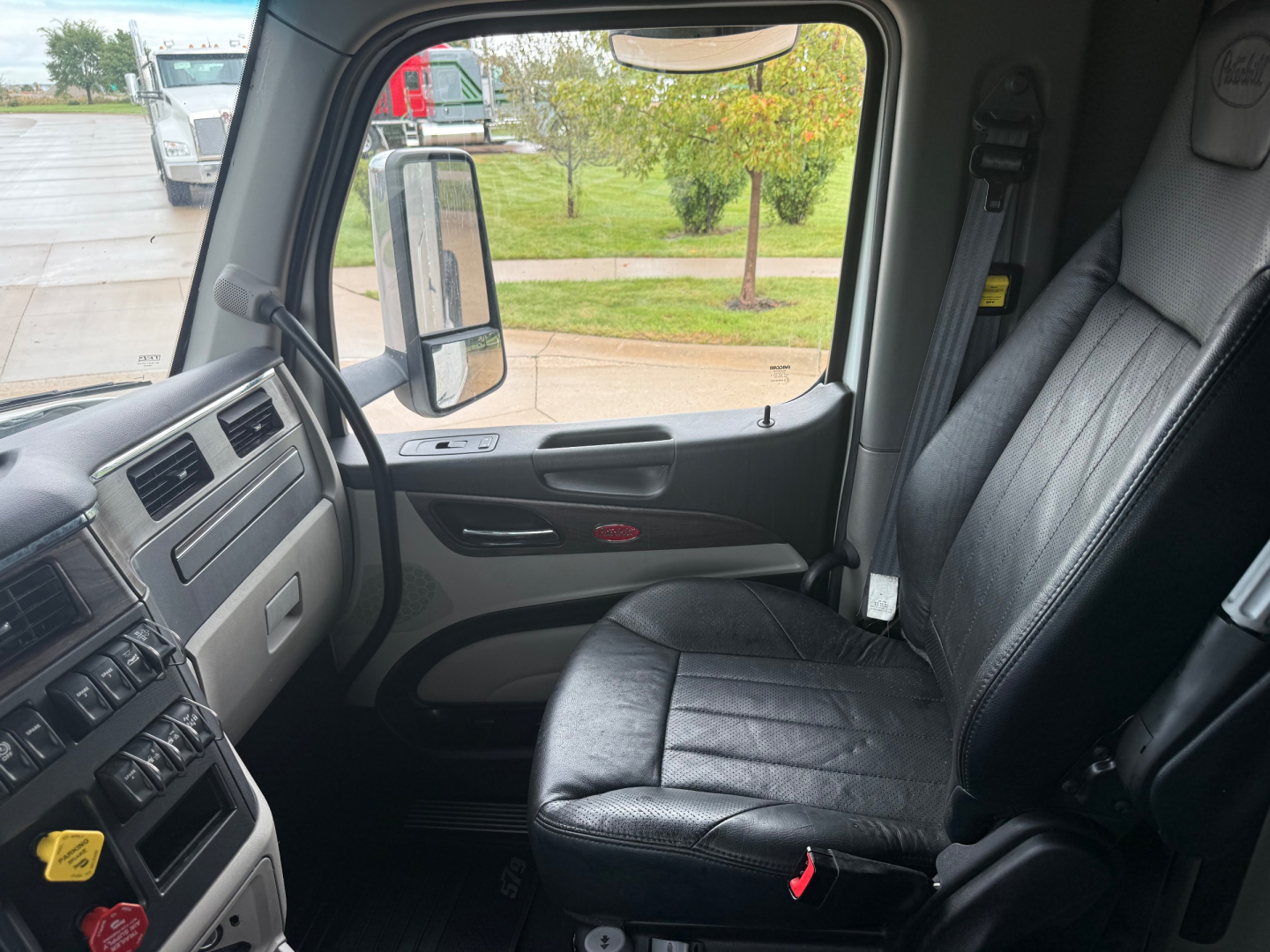 Interior of a 2023 Peterbilt 579 cab showing driver's seat and dashboard with side window and mirror visible.