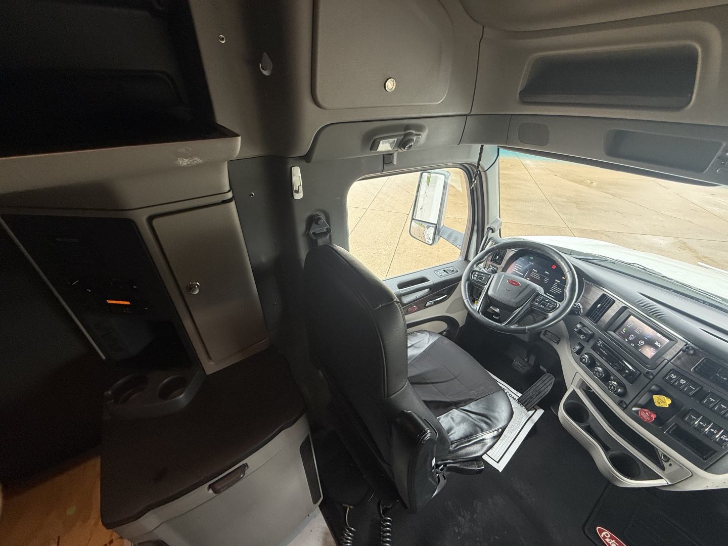 Peterbilt 579 cab interior showing driver seat and dashboard with steering wheel, center console, and overhead storage.