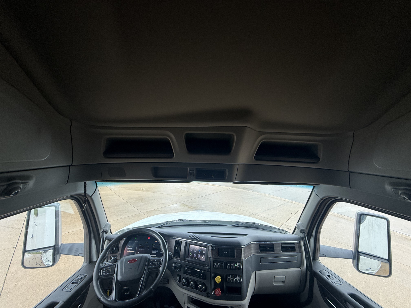 Peterbilt 579 cab interior view from driver seat showing dashboard, steering wheel, and dual side mirrors.