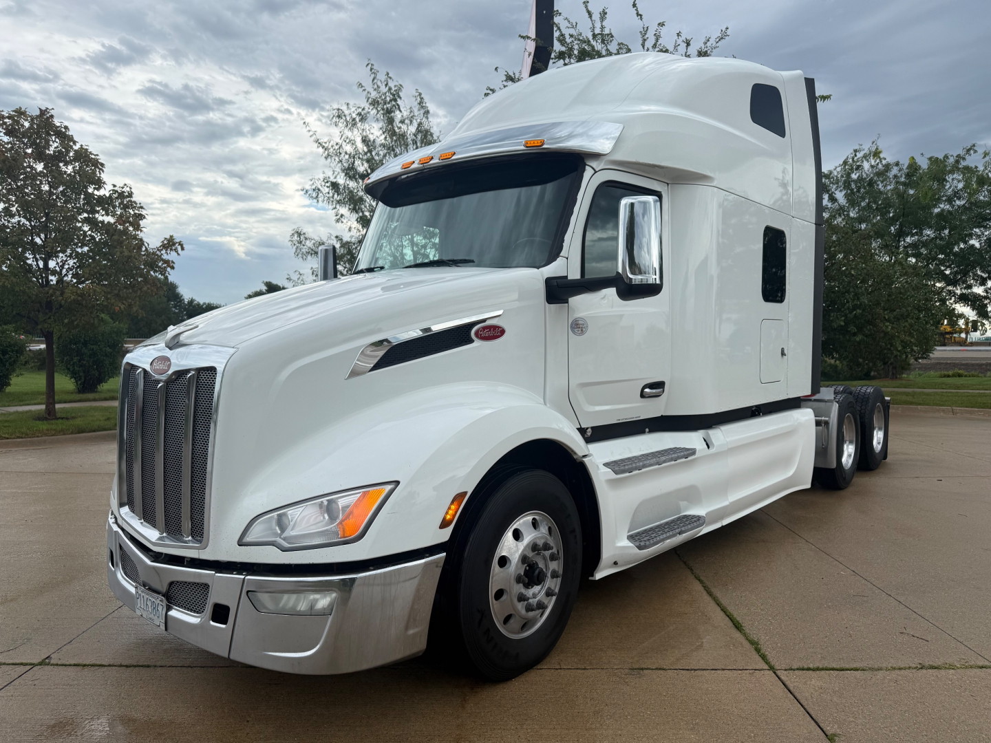Peterbilt 579 conventional sleeper truck in white, front three-quarter view, showing chrome grille, aerodynamic mirrors, and side steps.