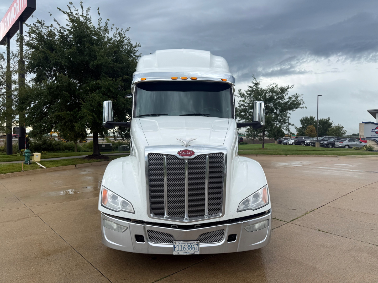 Peterbilt 579 front view in white with grille, headlights, and chrome mirrors. California license plate visible; cloudy sky.