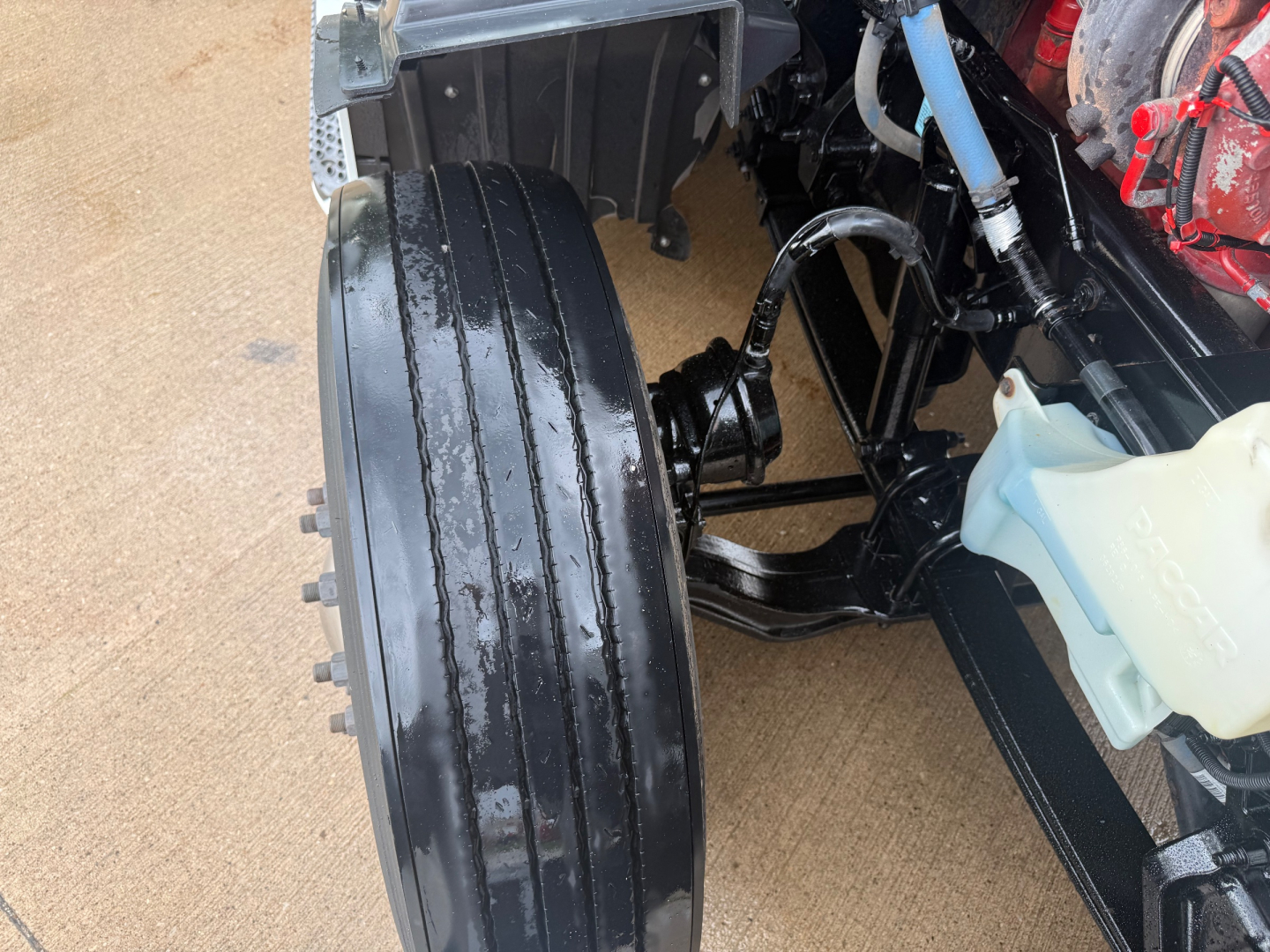 Truck front wheel area of a 2023 Peterbilt 579 conventional sleeper showing front fascia, wheel, and suspension components.
