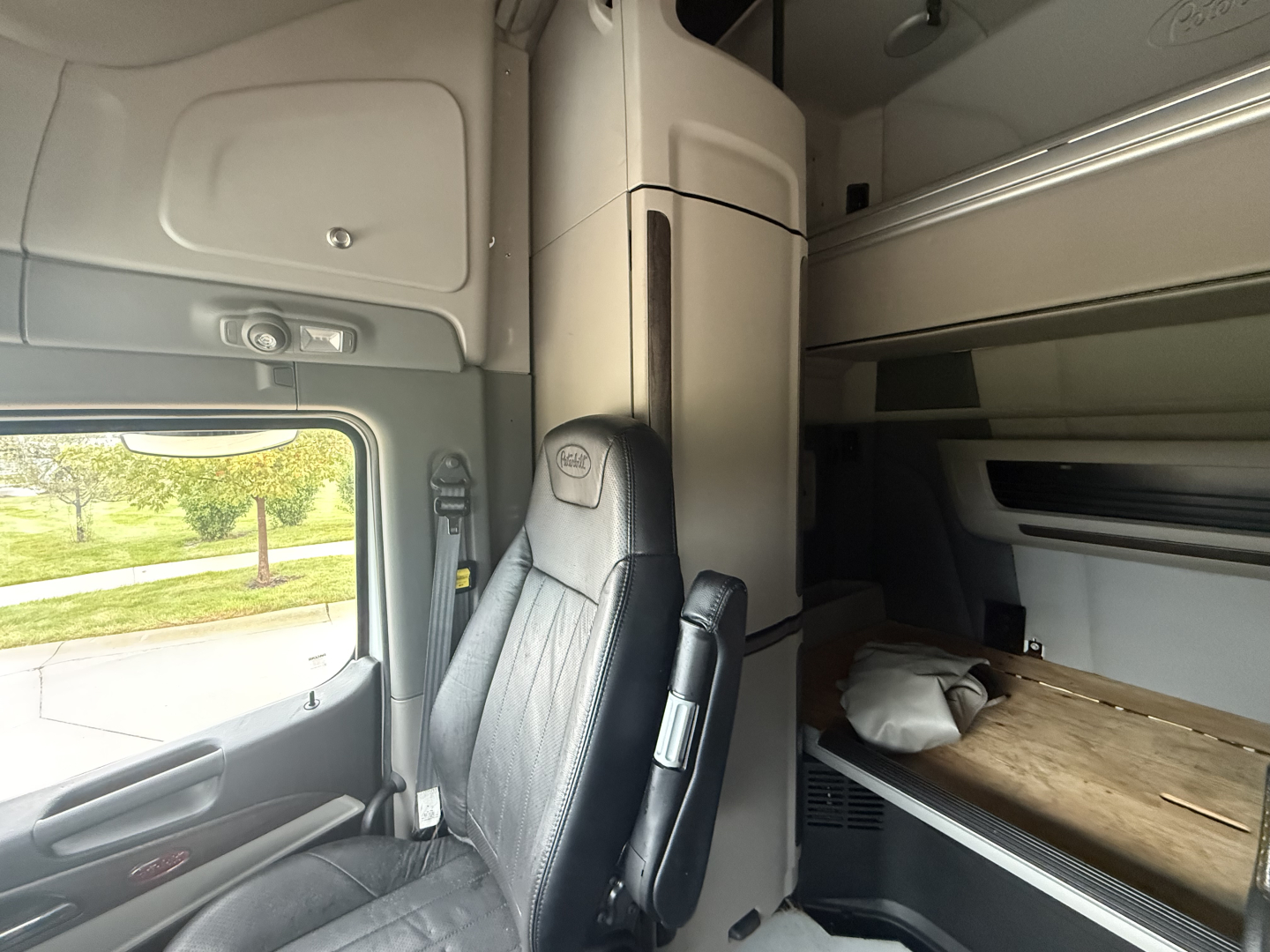 Peterbilt 579 sleeper cab interior showing driver seat and bunk area with overhead storage and side window.
