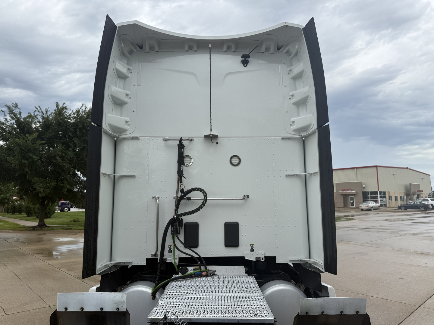 Peterbilt truck sleeper cab interior rear wall with wiring harnesses and circular access port, white paint, metal steps at bottom.