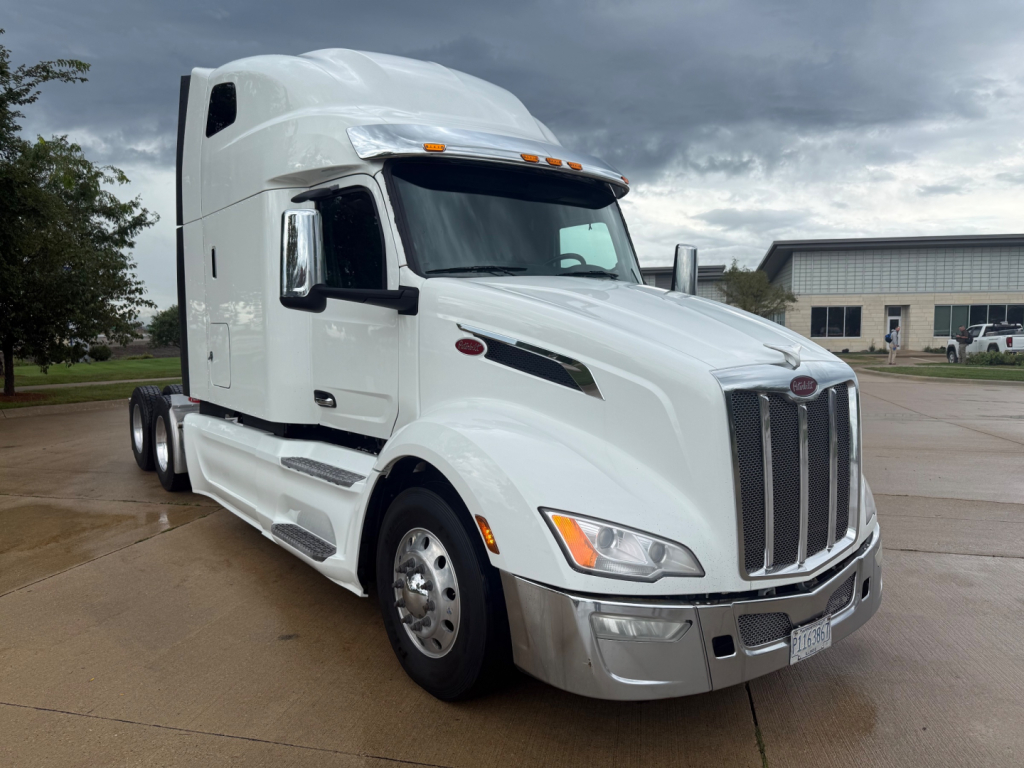 Peterbilt 579 tractor-trailer in white, front-left view showing chrome grille, headlights, and sleeper cab.