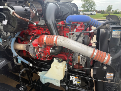 Peterbilt 579 engine bay showing red diesel engine, hoses, alternator, coolant reservoir, and air intake components.