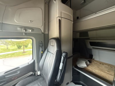 Peterbilt 579 sleeper cab interior showing driver seat and bunk area with overhead storage and side window.