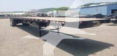 Flatbed trailer showing a long, low-profile deck with tandem axles and support legs visible; dealership watermark overlapped.
