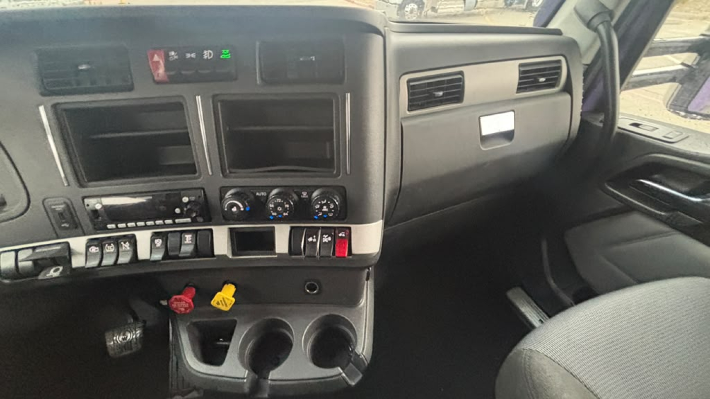 Kenworth truck dashboard with control switches and cup holders visible; front console area showing climate controls, empty screen slots, and dashboard details.