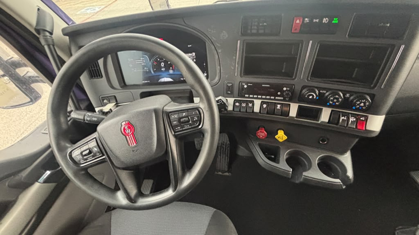 Interior of a Kenworth T680 cab showing steering wheel, dashboard, and center console with gauges and controls.