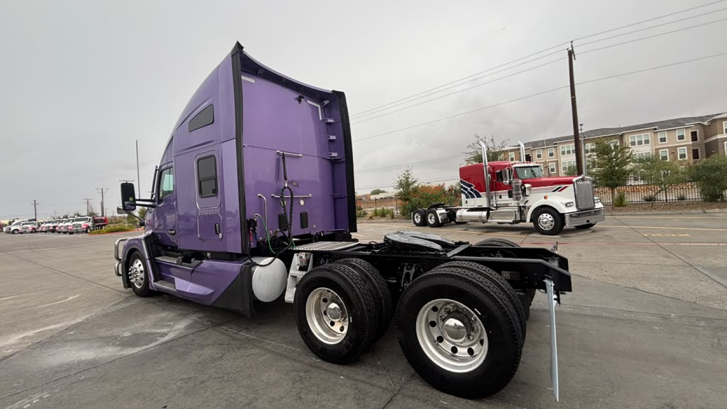Kenworth T680 tractor in purple cab and black chassis, 2 rear axles, side view showing sleeper cab and fuel tanks.