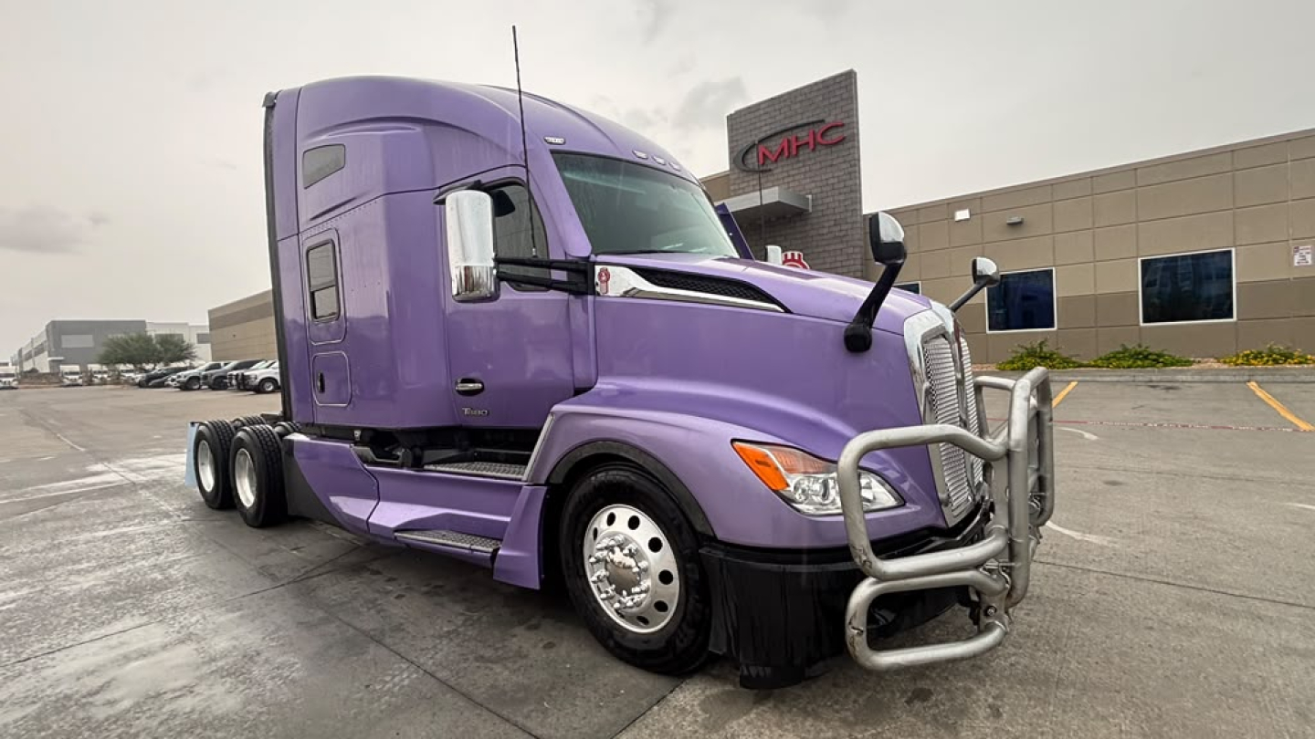 Kenworth T680 truck in purple showing front bumper guard and cab, side mirror, and wheel, with dealership in background.