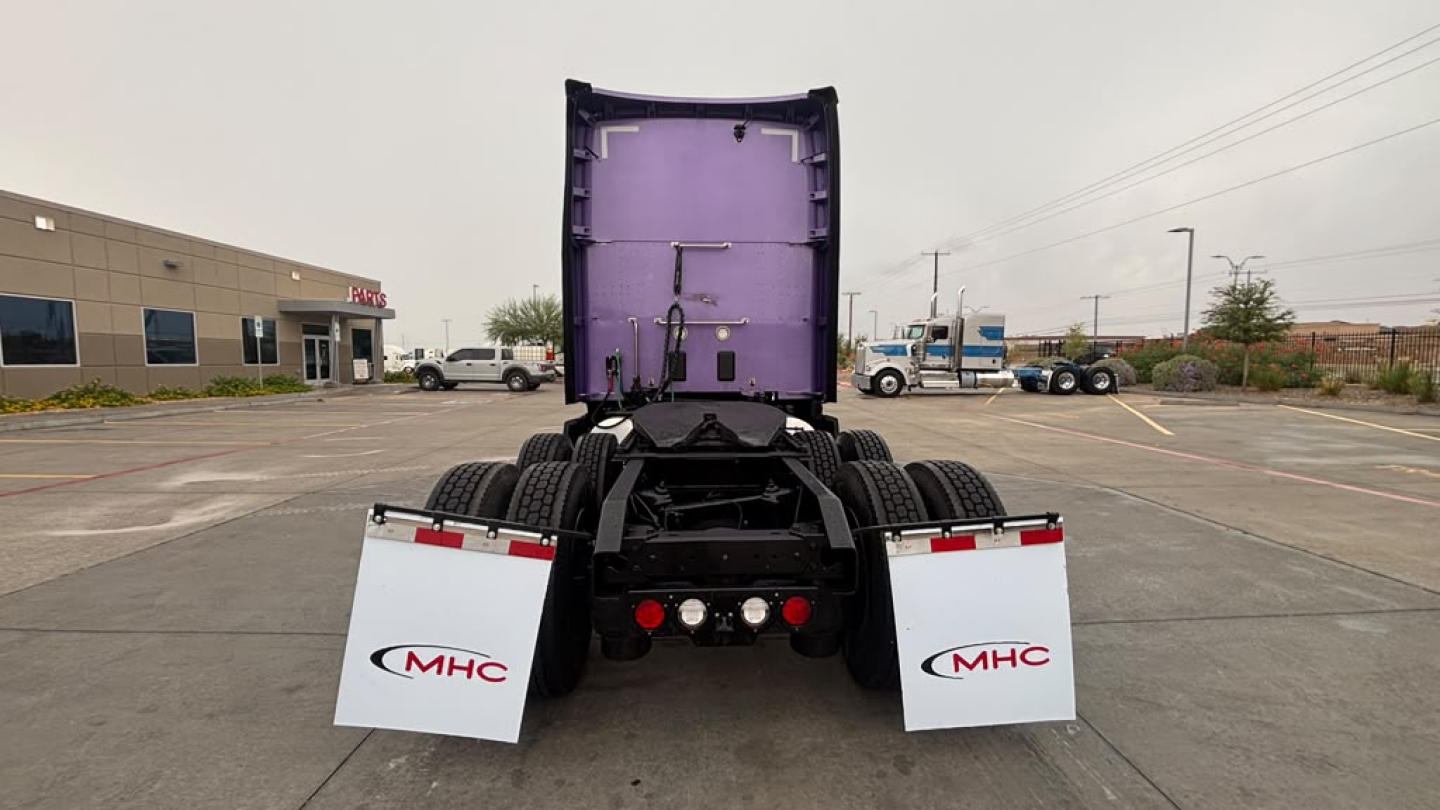 Rear view of a Kenworth tractor chassis with purple sleeper cab, fifth wheel, and MHC mud flaps. VIN plate not visible; no engine details.