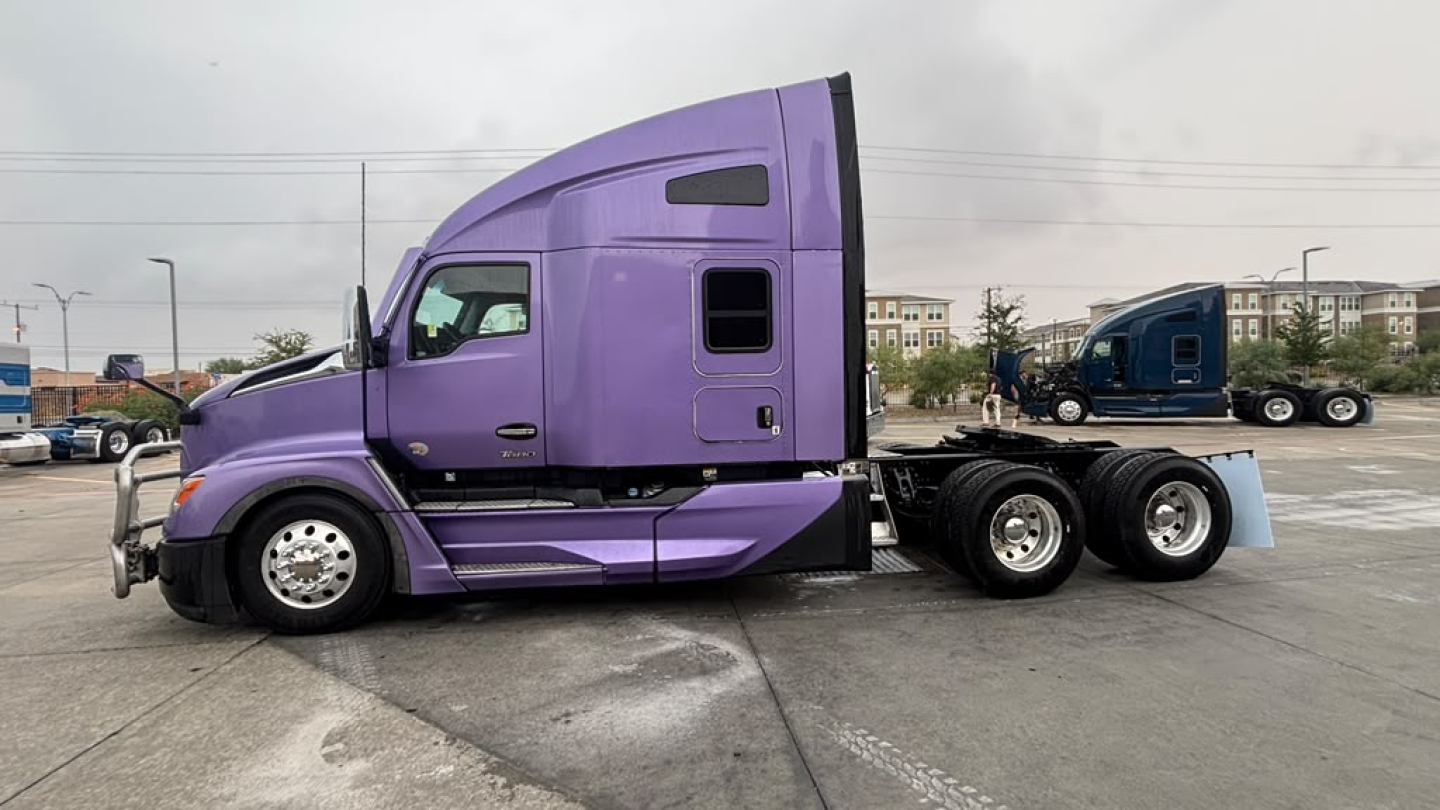 Purple 2024 Kenworth T680 sleeper cab tractor side view showing long wheelbase and triple rear axles.