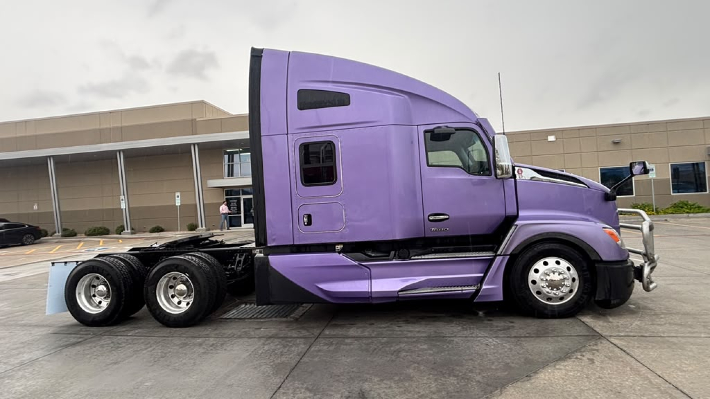 Side view of a purple 2024 Kenworth T680 conventional sleeper truck, 6x2 rear, with triple rear axles and chrome wheels.