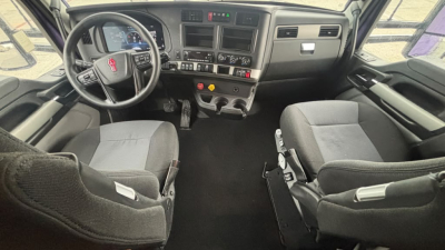 Kenworth T680 truck cab interior showing steering wheel, dashboard, and two front seats. Text on dash includes gauges and controls, with center console and gear shifter visible.