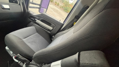 Kenworth T680 interior showing front seat and driver-side door area in view passenger seat not visible. Textured fabric seat, steering wheel edge, door panel, and window. 