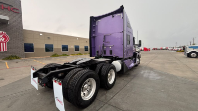 Kenworth T680 tractor with purple sleeper cab and dual rear axles, viewed from rear-left in a truck lot.