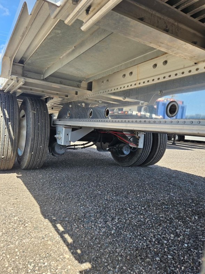 Semi-trailer undercarriage showing tandem axles and suspension with metal drop deck frame and support beams.