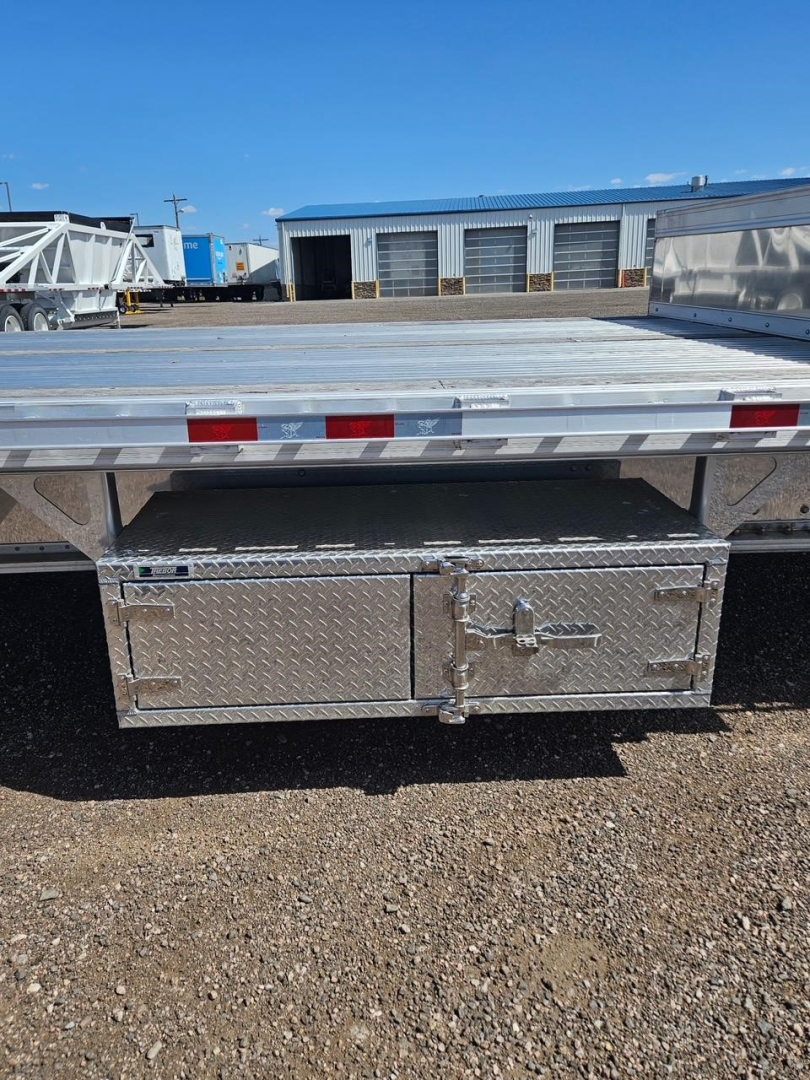 Trailer rear with diamond plate toolbox mounted under drop deck showing latch handles and reflective tape along edge.
