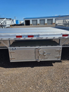 Rear view of a 2026 Manac Darkwing 53' Drop Deck trailer showing underbody toolbox/ storage box with diamond plate pattern, latch handles, and reflective tape on the edge.