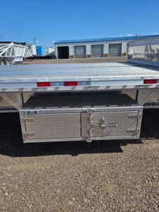 Trailer rear with diamond plate toolbox mounted under drop deck showing latch handles and reflective tape along edge.