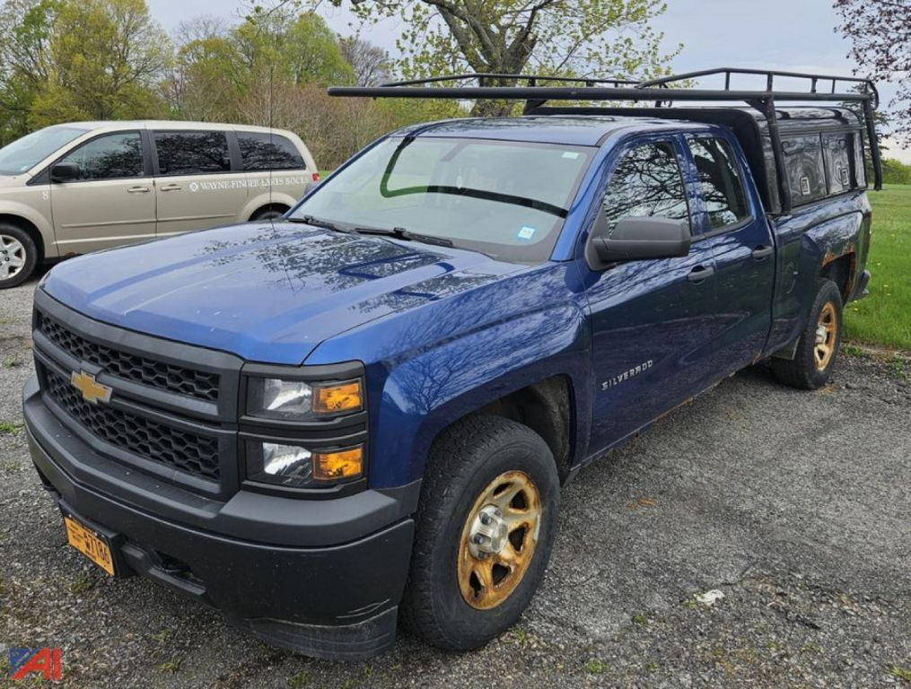 Chevrolet Silverado 1500 pickup truck with cap in blue, front three-quarter view, black grille, yellow wheels, roof rack, parked on gravel.