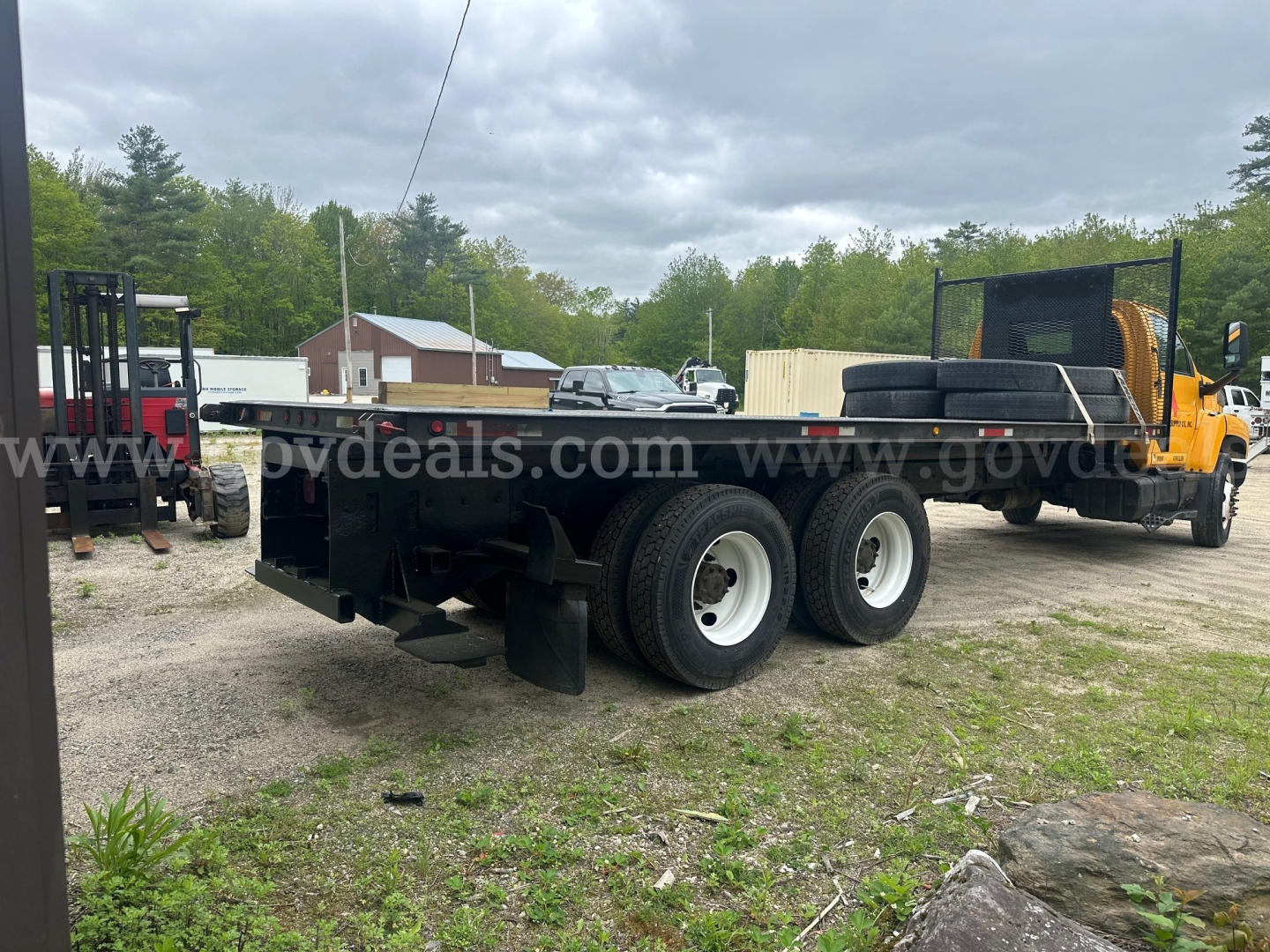Flatbed truck chassis with dual rear axles and a GMC C8500, 2006 model, on a gravel lot.