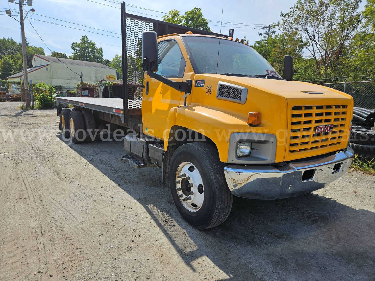 GMC C8500 flatbed tow truck in yellow with black flatbed, front grille, large side mirrors, and warning lights. VIN 1GDT8C4C56F417000 visible on listing.