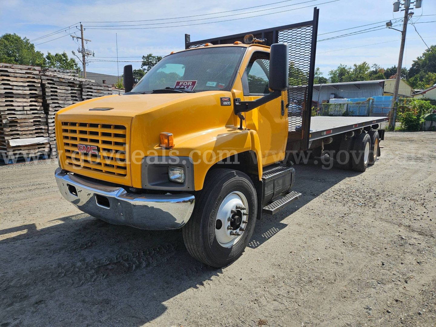 GMC C8500 flatbed truck in-service showing yellow cab and long flatbed with metal headache rack and dual rear wheels.