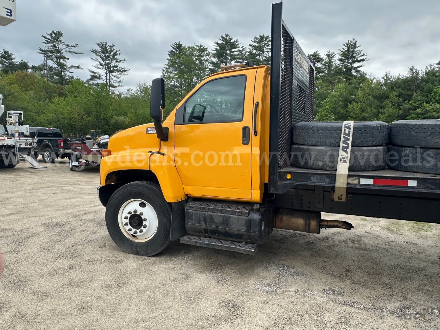 GMC C8500 flatbed truck in yellow with black flatbed. Side view shows cab, door, window, black step, and spare tire mounted on bed. VIN and stock number not visible on image.