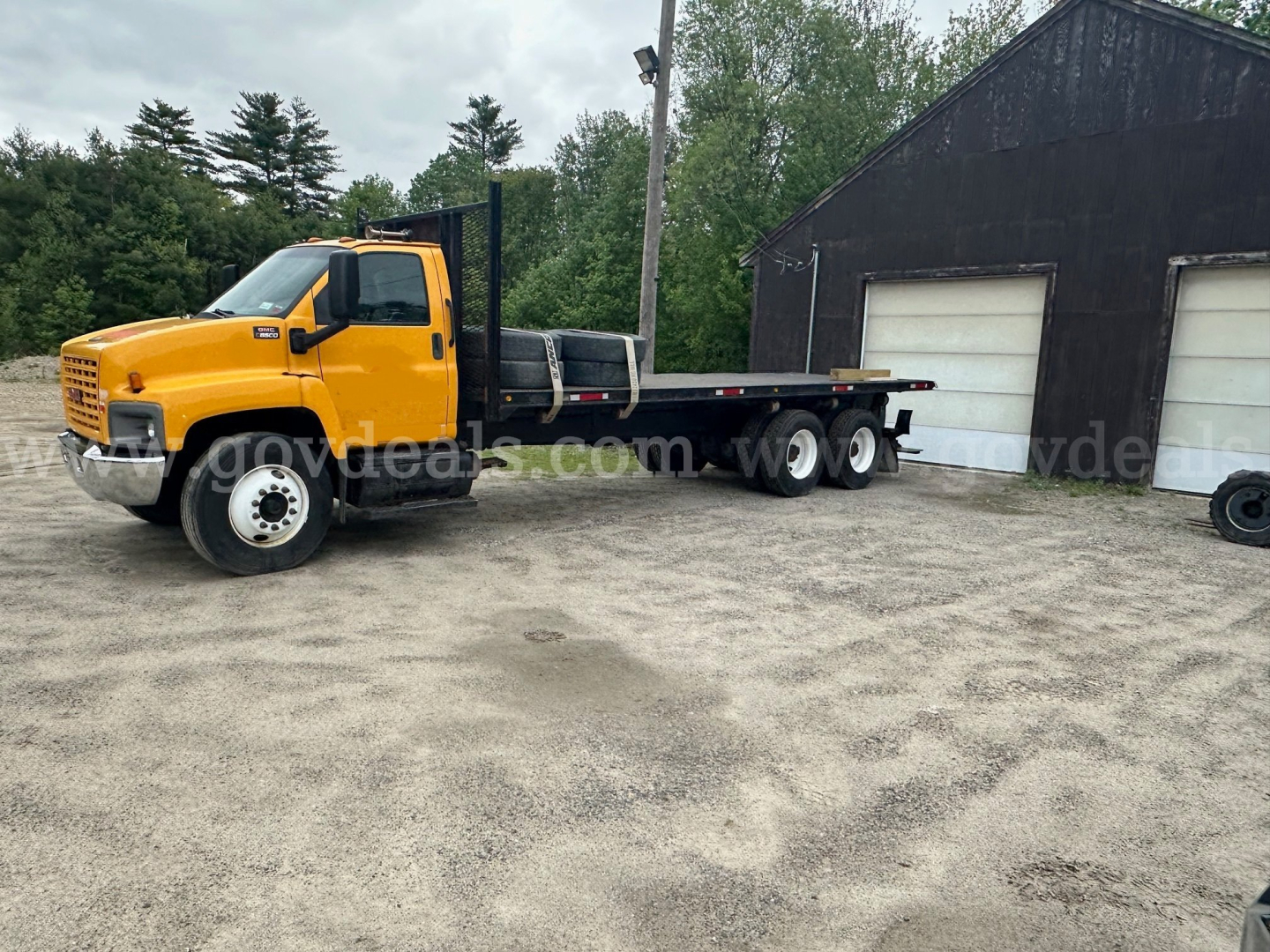 GMC C8500 flatbed truck showing a yellow cab and black flatbed parked outdoors near a dark building.