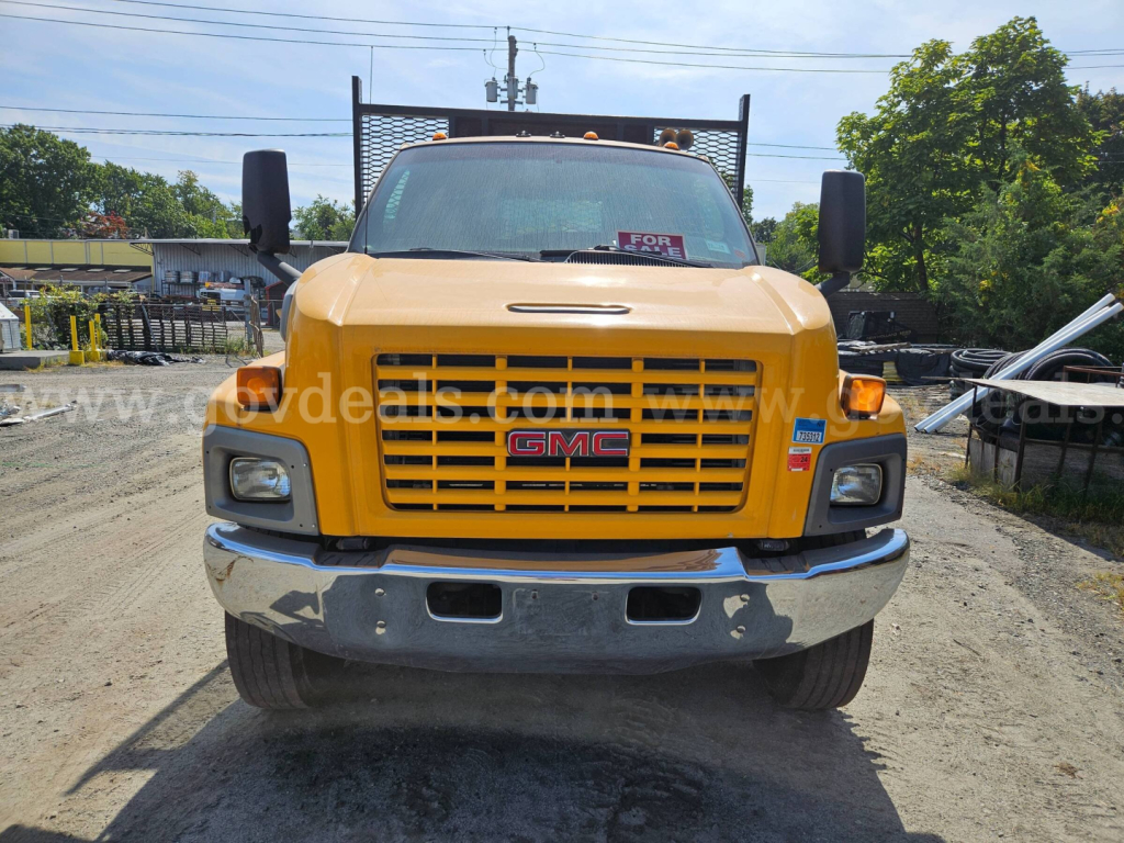 Front view of a yellow 2006 GMC C8500 flatbed truck with grille, headlights, bumper, and tow mirrors.