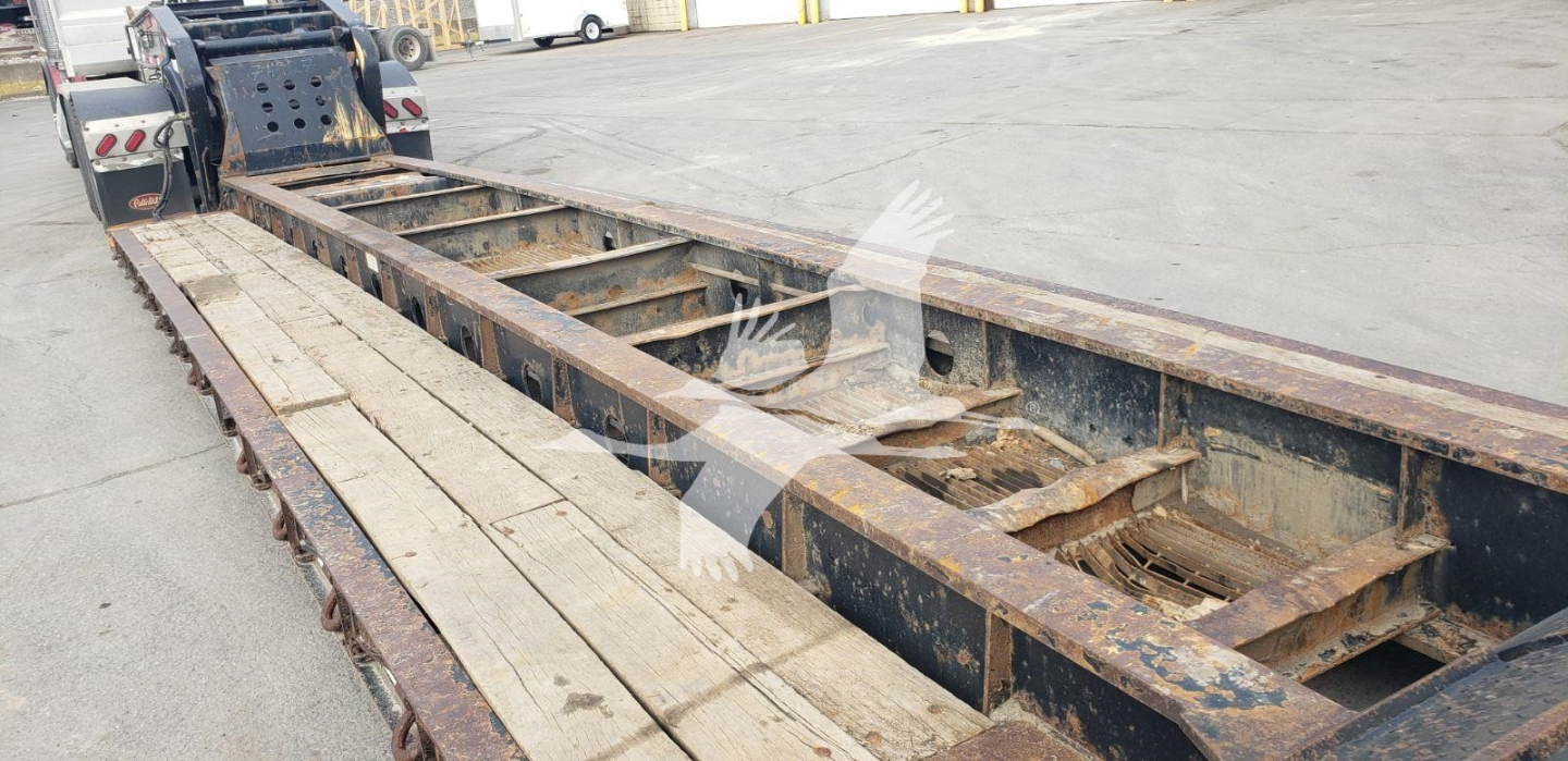 Trailer frame with long flatbed/lowboy, metal beams and wooden decking, rusty in-service condition, Fontaine brand 55H-DSR trailer visible.