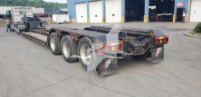 Lowboy trailer with multiple axles, rear view showing tires and deck; some markings and lights visible on rear bumper.