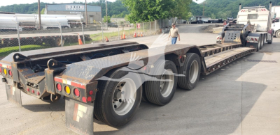 Fontaine trailer showing 55H-DSR model, long lowboy flatbed with triple axle undercarriage and rear lights. Visible tires and chain links, stock lot in background.