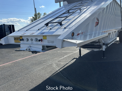 Trailer bed showing hydraulic tailgate and side panels with warning labels, in-service white aluminum dump trailer with support legs deployed.