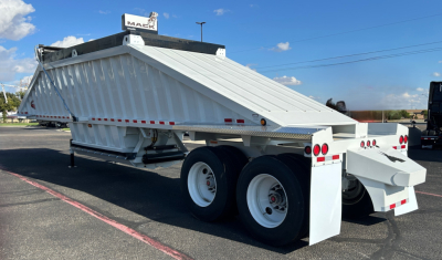 Dump trailer with tandem axles and high-side dumping body showing sloped side panels and rear ramp in serviceable condition.