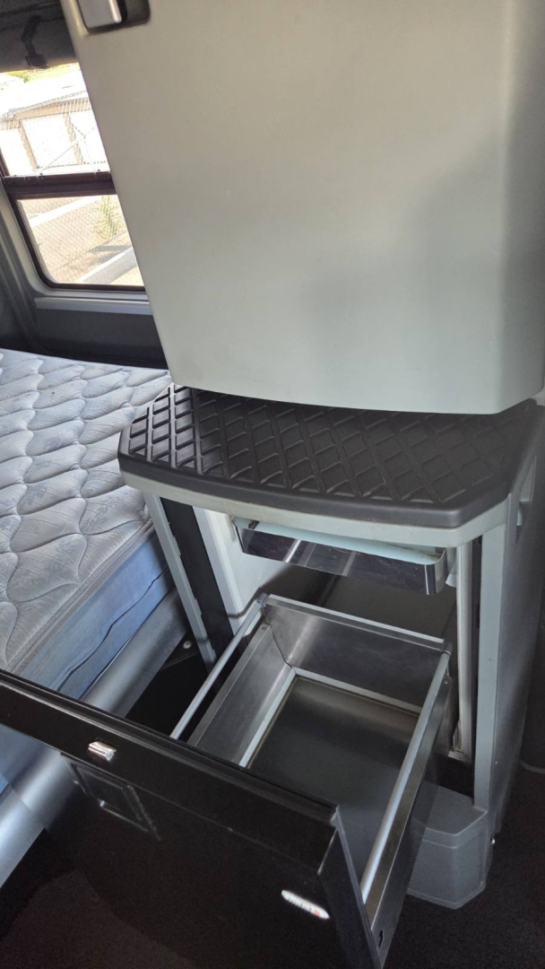 2017 Kenworth T680 sleeper cab interior showing a storage drawers and a small step, with a quilted bed surface and overhead cabinet.