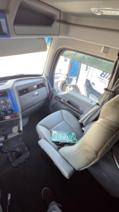 Kenworth T680 interior cab view showing steering wheel, dashboard, and passenger seat with a license plate on the seat.