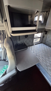 Cab interior of a Kenworth T680 sleeper shows upper bunk/closet area and a folding desk with quilted sleeper upholstery.