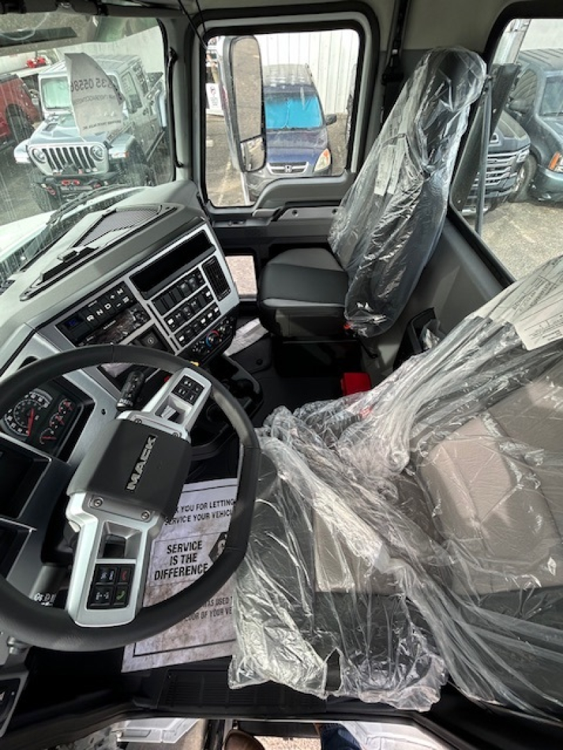 Cab interior of a new 2026 Mack GR64B vacuum tank truck showing steering wheel, dashboard with controls, and plastic-wrapped driver and passenger seats.